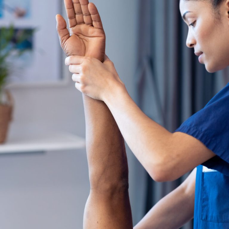 Vertical of diverse female physiotherapist treating arm of senior male patient, copy space. Hospital, medical and healthcare services.